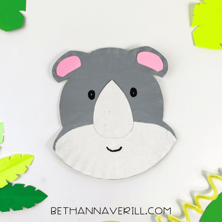 The completed rhino paper plate craft surrounded by green and yellow jungle-style paper leaves.