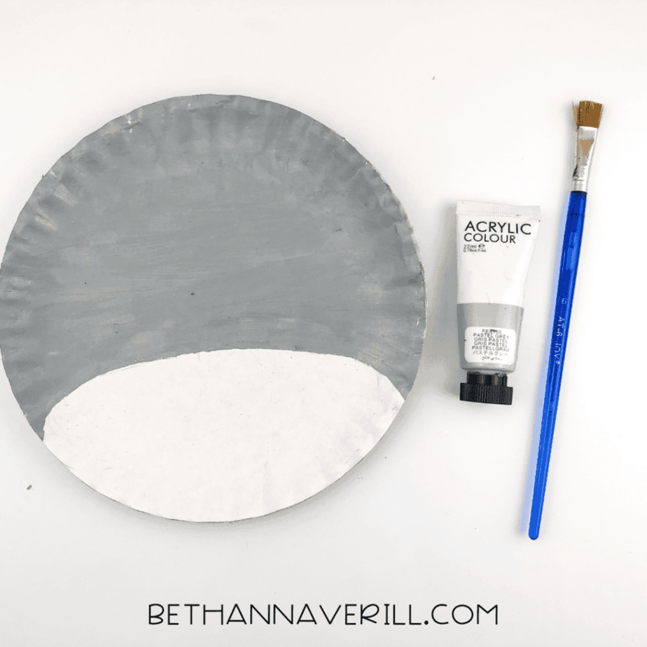 A paper plate with the top three-quarters painted gray and the bottom left unpainted to create a snout area.
