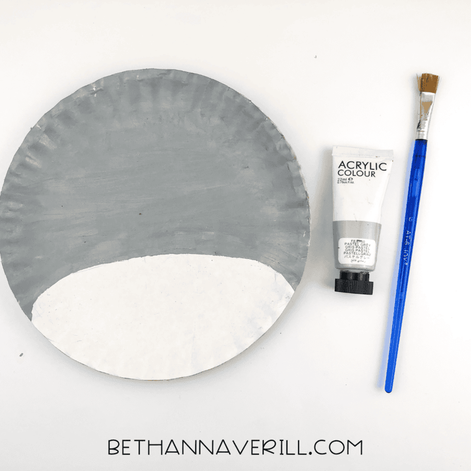 A paper plate with the top three-quarters painted gray and the bottom left unpainted to create a snout area.