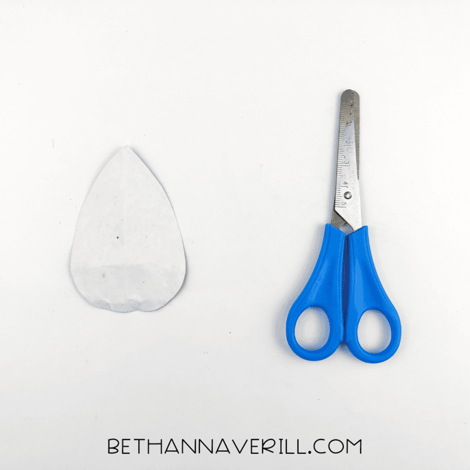 A white paper teardrop shape cut and shown beside scissors, ready to be used as the rhino’s horn.