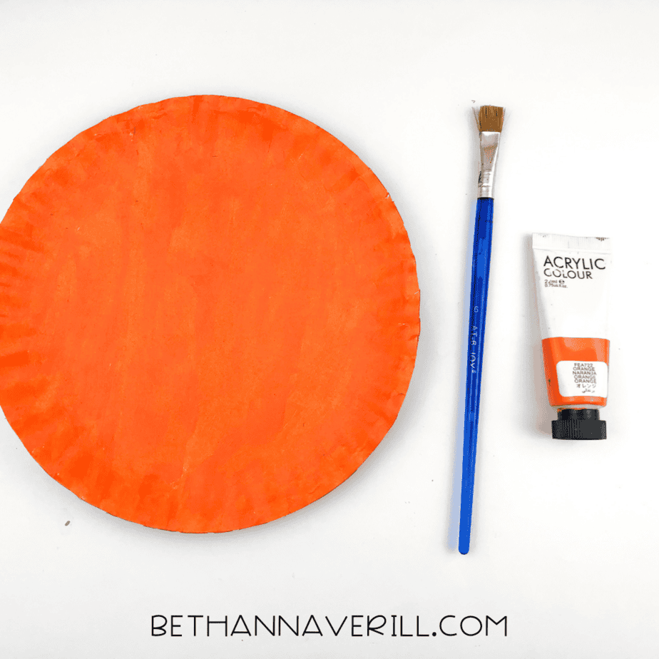 An orange paper plate with a brush and paint.