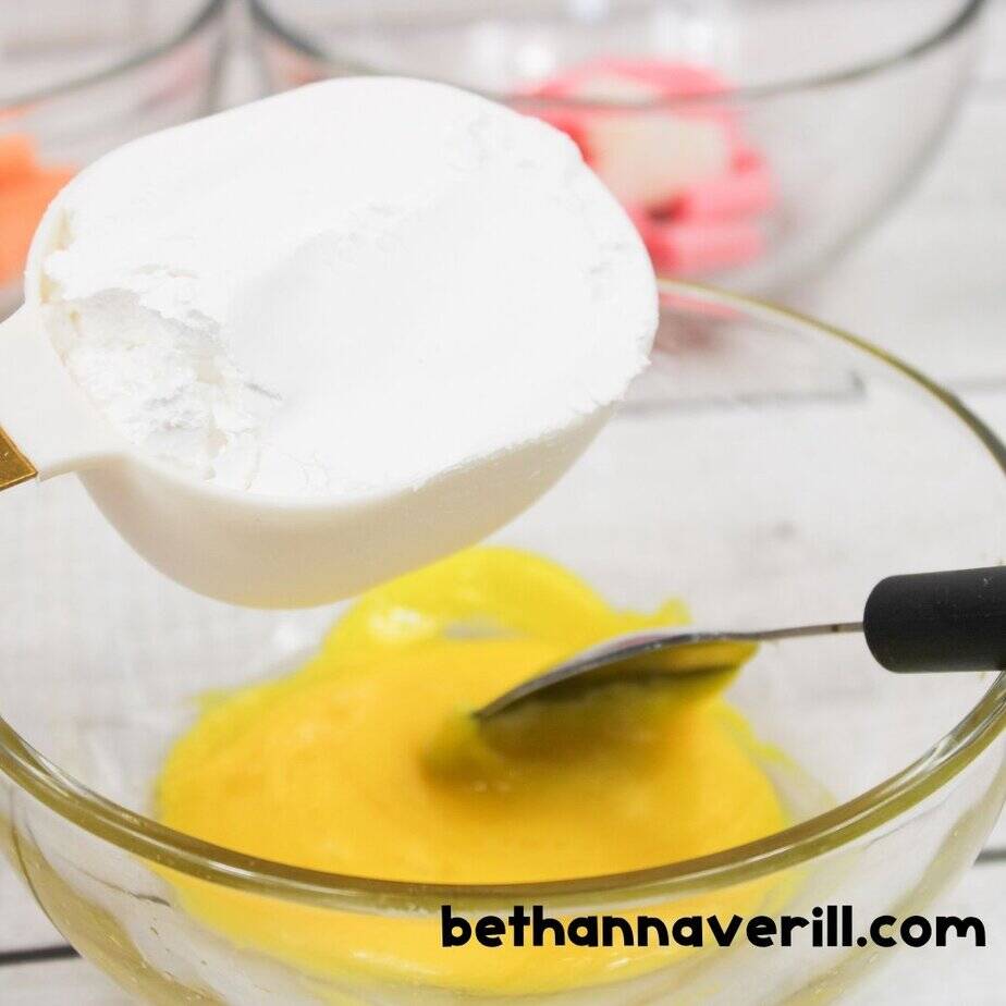 Adding powdered sugar to melted yellow Starburst mixture in a bowl to create edible Starburst slime.