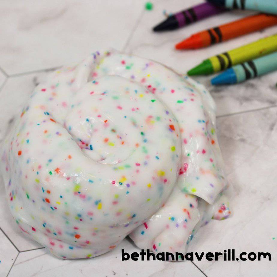 Swirled crayon slime with rainbow crayon shavings on a marble surface, surrounded by colorful crayons.