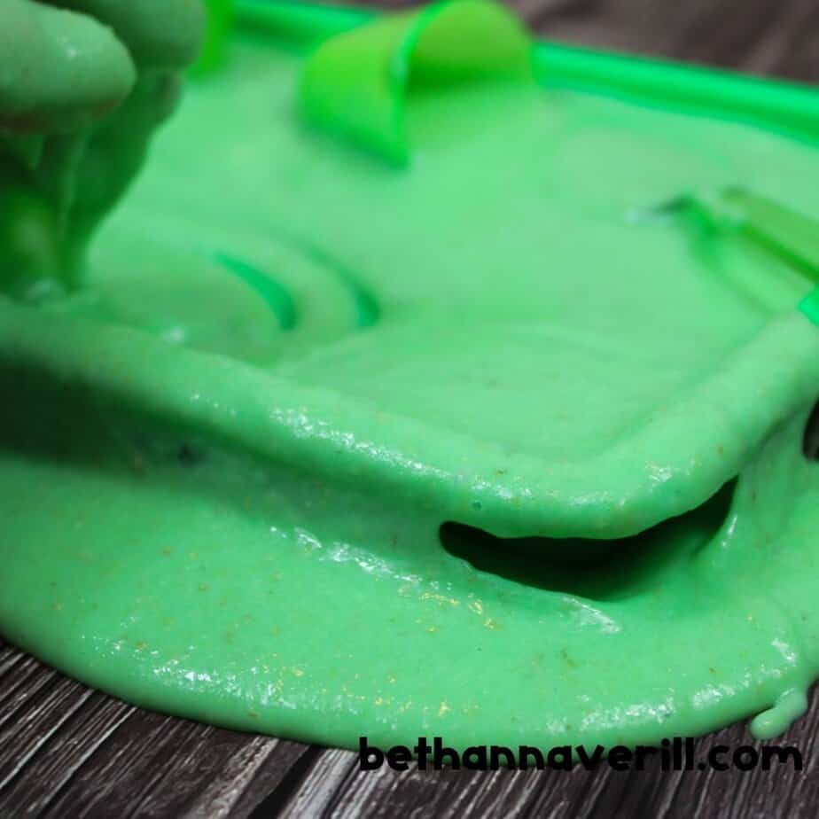 Close-up of Nickelodeon slime spreading out onto a wooden surface from a green tray, showing its gooey texture.