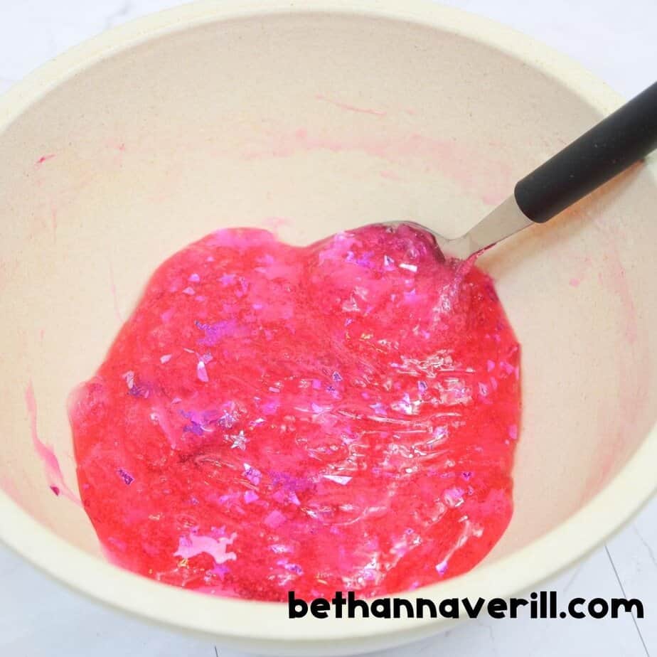 Unicorn slime in a bowl with spoon, fully mixed with pink color and glitter, ready to be kneaded as it pulls away from the sides.