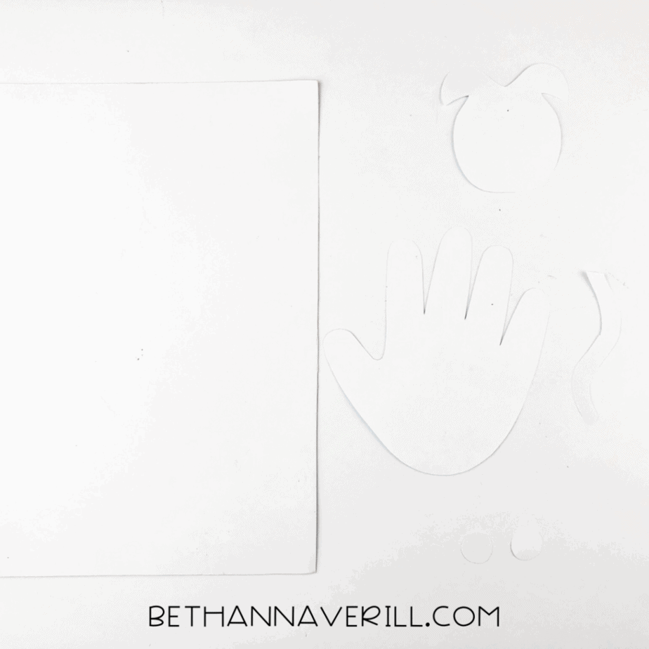 White template pieces cut out for the cow: head, ears, tail, eyes, and handprint.