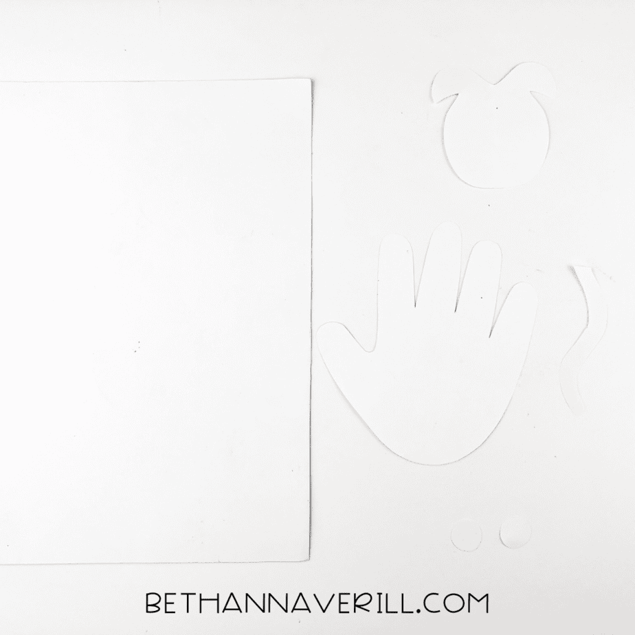 White template pieces cut out for the cow: head, ears, tail, eyes, and handprint.