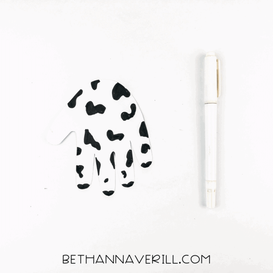Handprint colored with black spots to resemble a cow's pattern.
