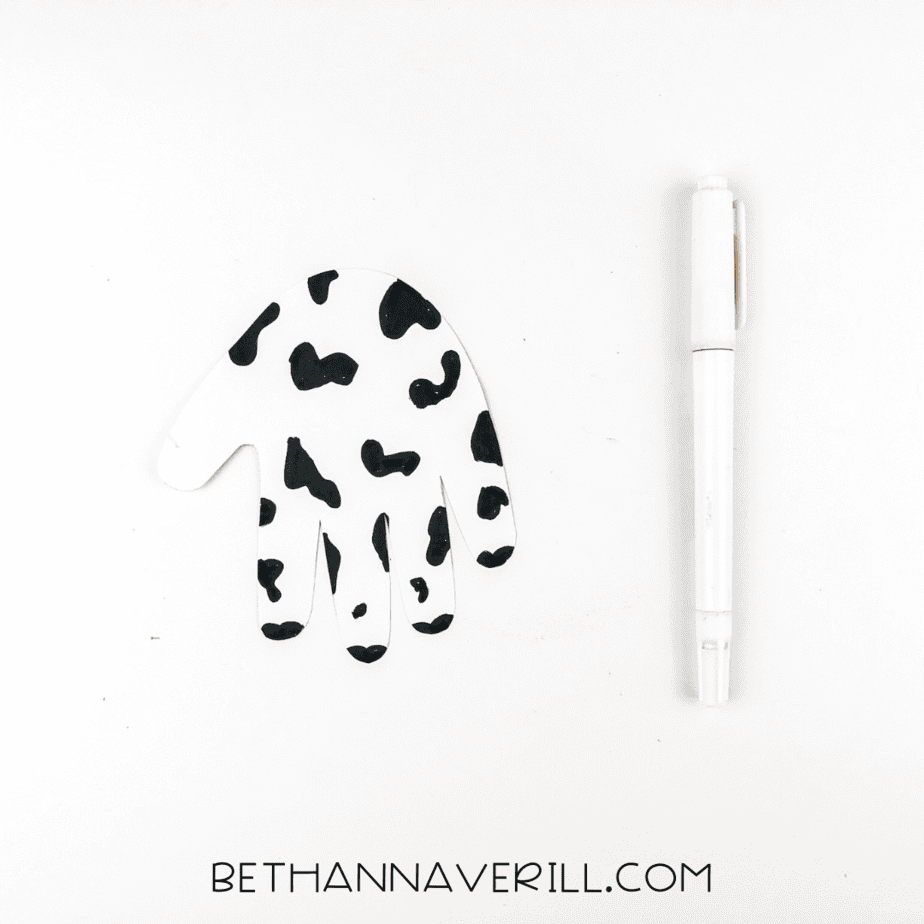 Handprint colored with black spots to resemble a cow's pattern.