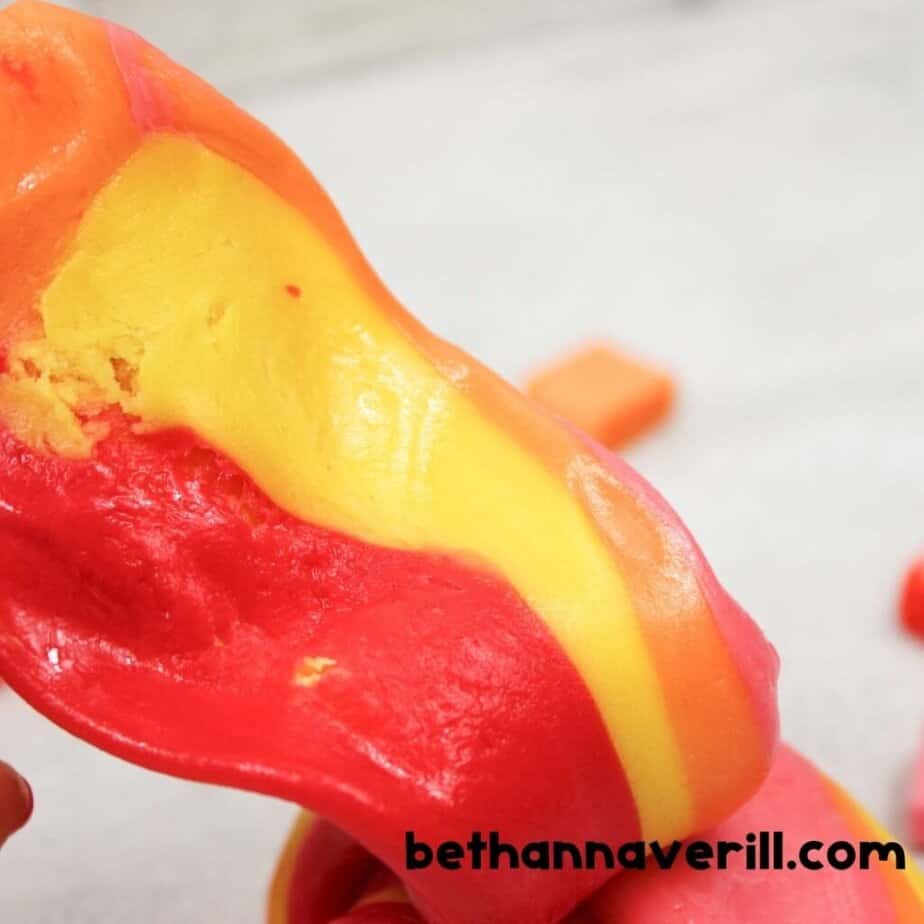 Stretchy red, yellow, and orange edible Starburst slime twisted together, showing its smooth texture and vibrant color.