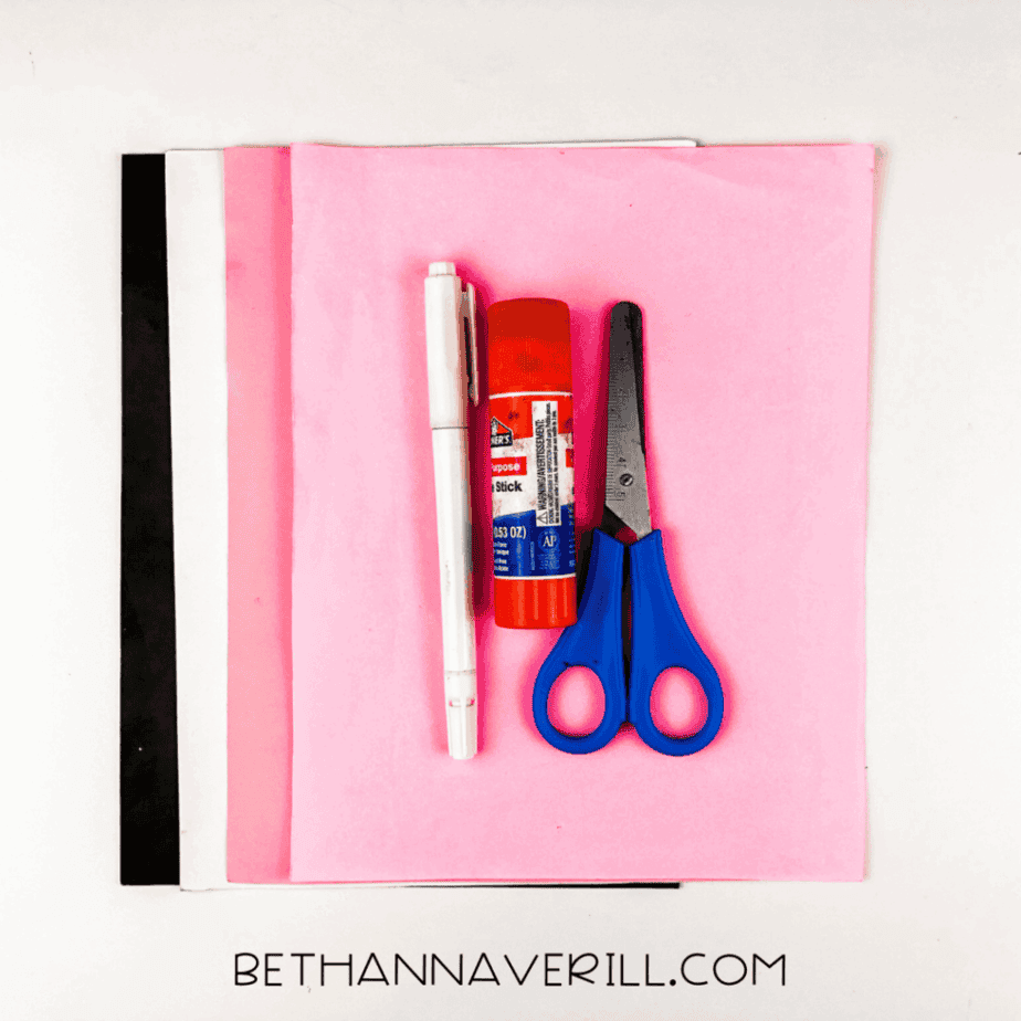 Craft supplies laid out: pink, white, and black construction paper, pencil, glue stick, and scissors.