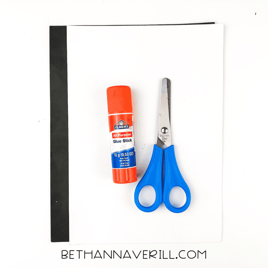 A glue stick, scissors, black construction paper, and white construction paper laid out on a white surface.