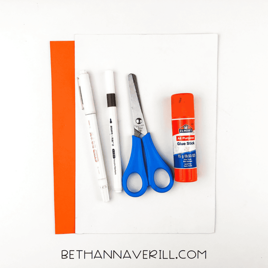 Glue stick, scissors, pens, and orange and white paper laid out for giraffe handprint craft.