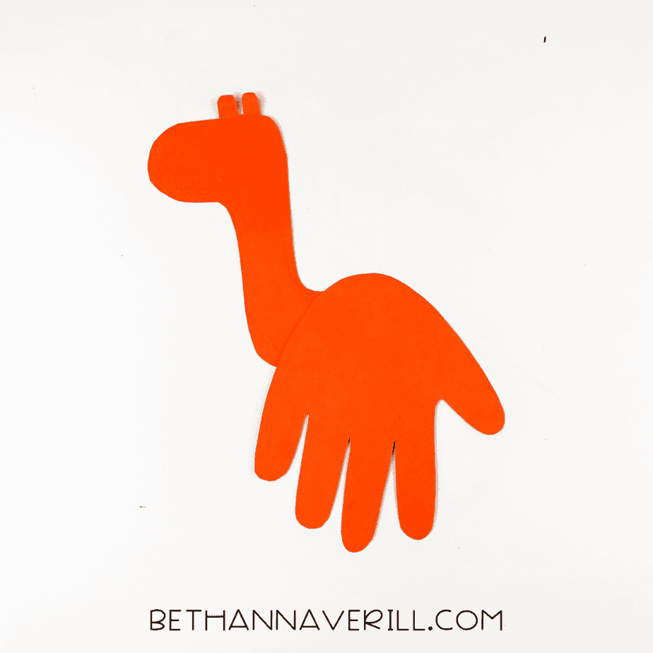 Orange handprint glued to giraffe neck to form body shape.