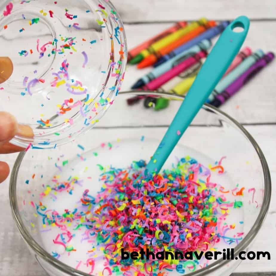 Mixing vibrant crayon shavings into a bowl of white glue mixture to make fun and colorful crayon slime for kids.