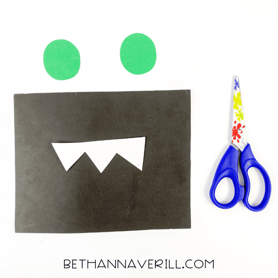 Black paper with white zigzag teeth cut out and two green paper circles for the alligator’s eyes.
