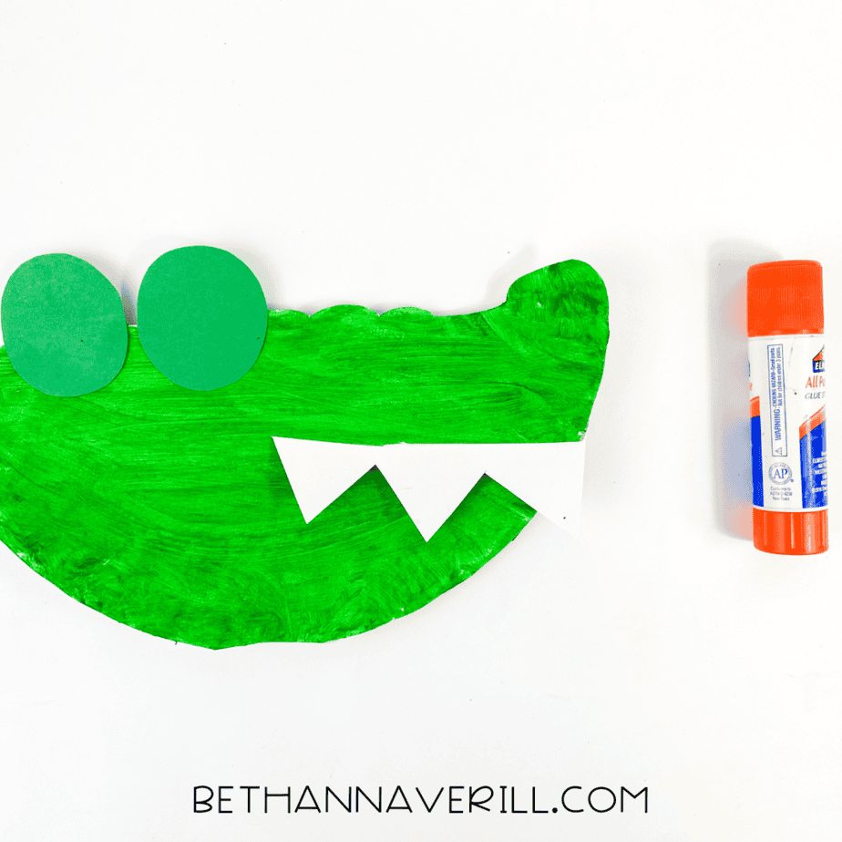 Green alligator head with paper eye shapes and zigzag teeth glued on, ready for more details.