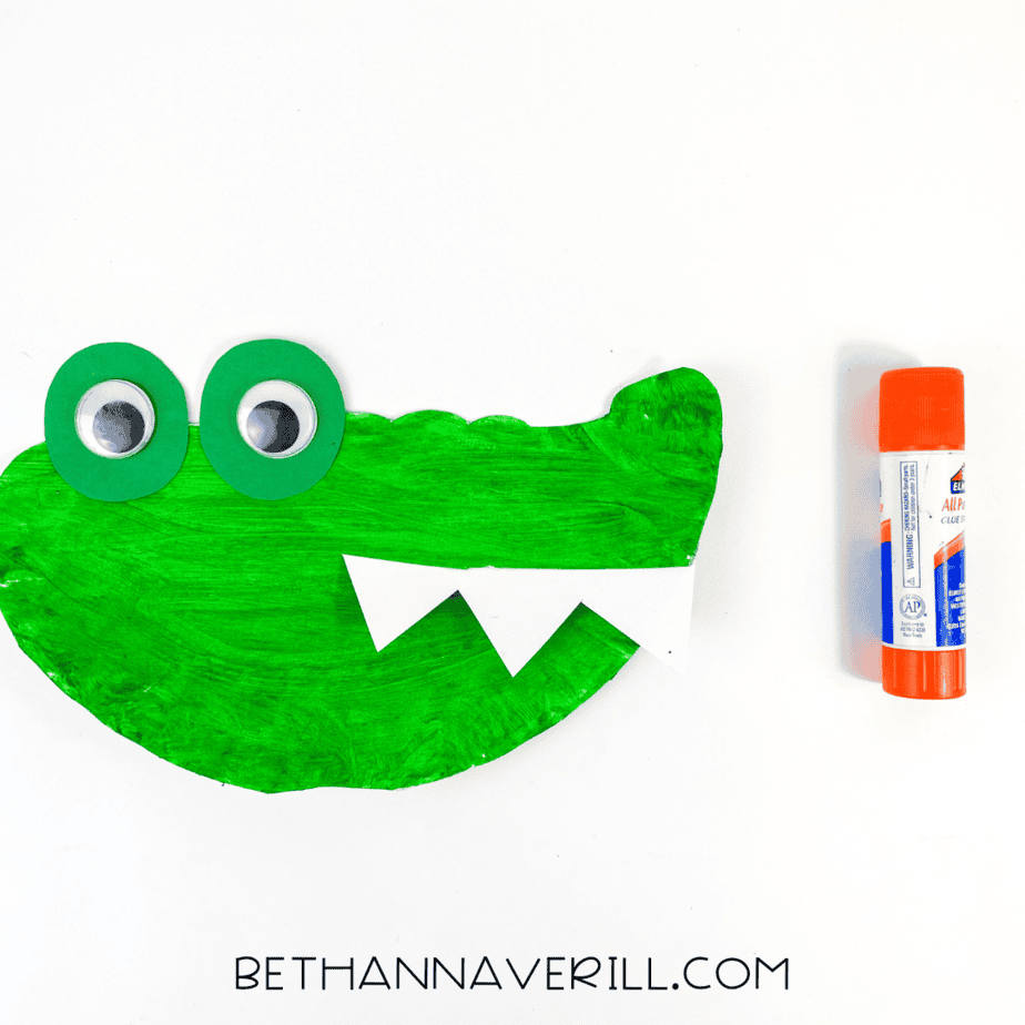 Googly eyes added on top of the green eyelid shapes, bringing the alligator face to life.