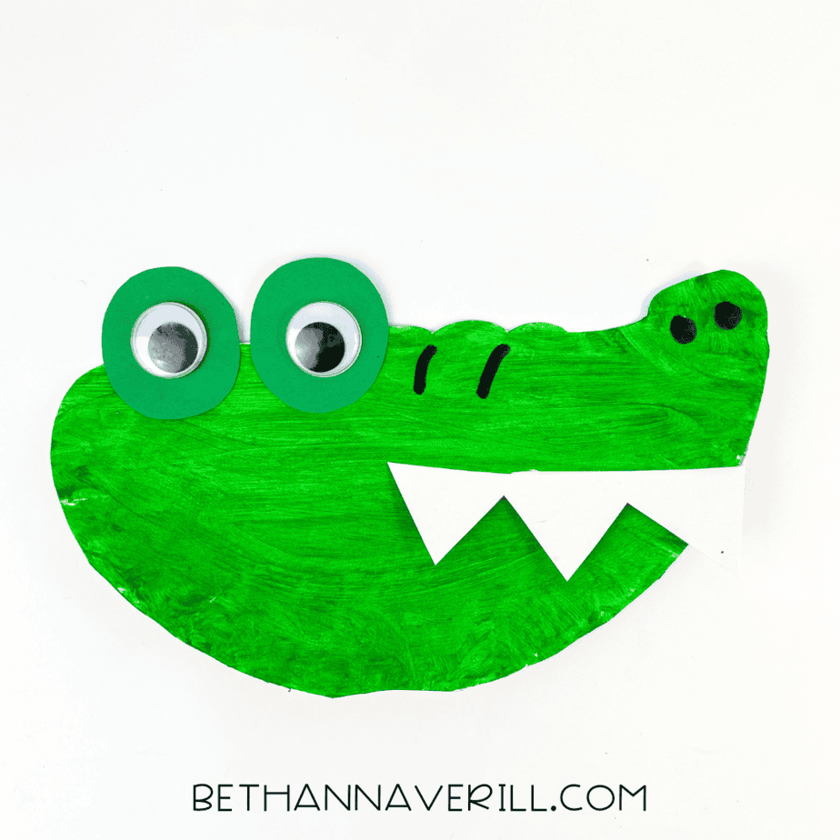 Completed paper plate alligator craft with big eyes, sharp white teeth, and a silly expression.