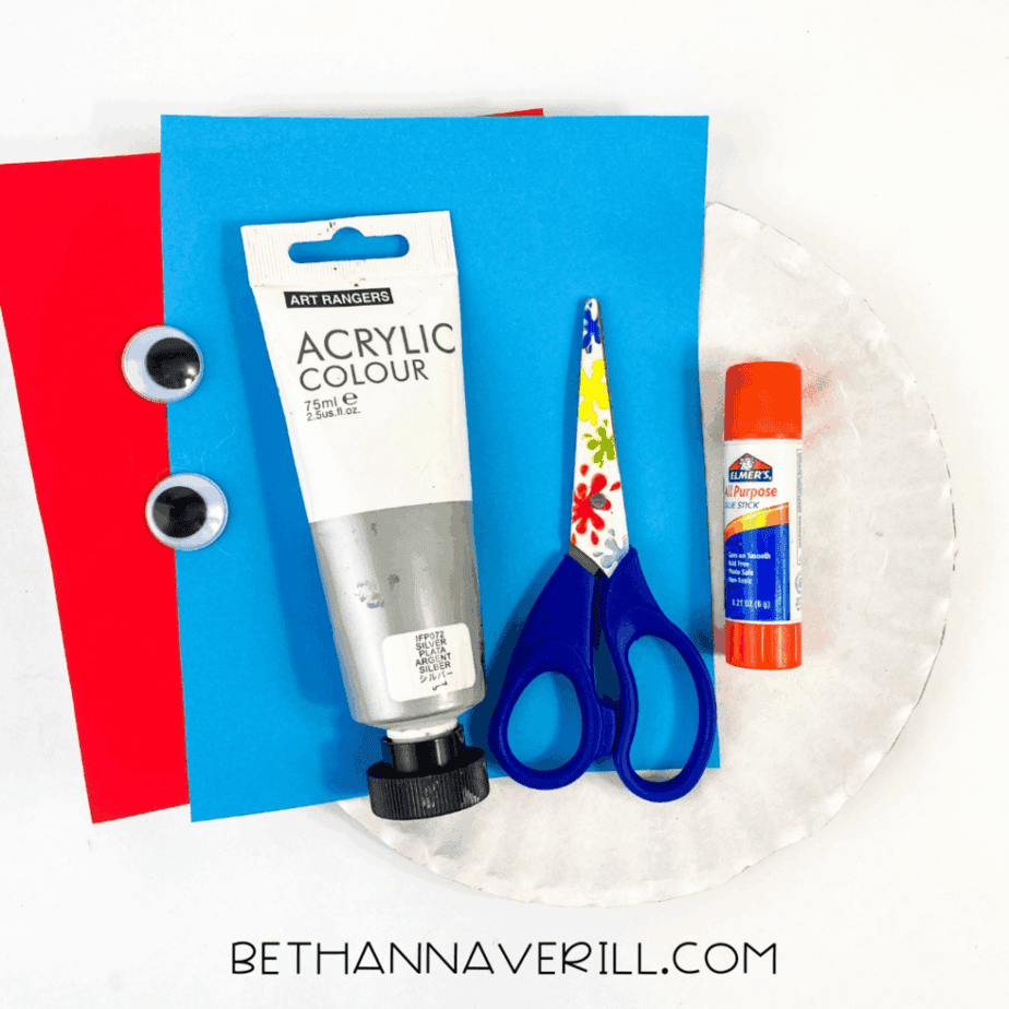 Supplies needed for baboon paper plate craft, including glue stick, googly eyes, acrylic paint, scissors, and construction paper.