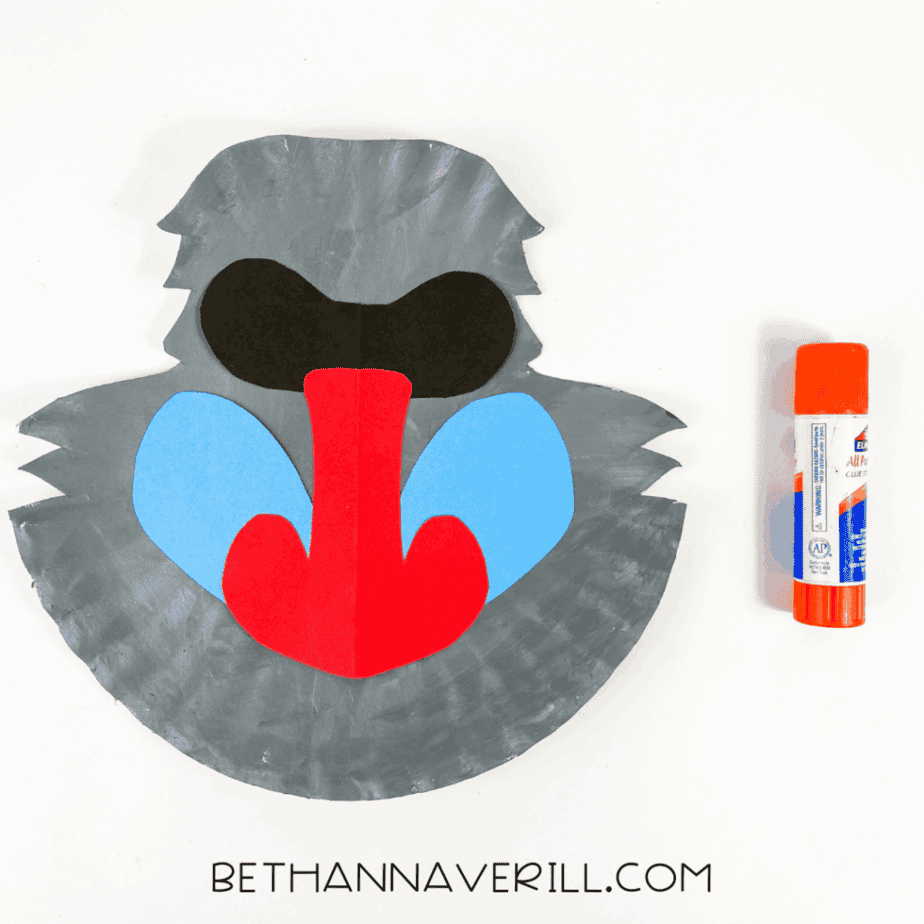 Grey paper plate with the baboon's red nose, blue cheeks, and black eye mask glued on.