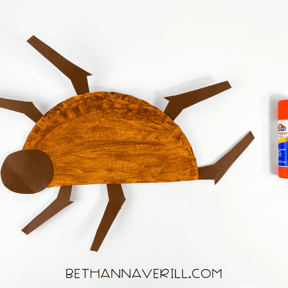 Brown paper plate half with legs and head glued in place.