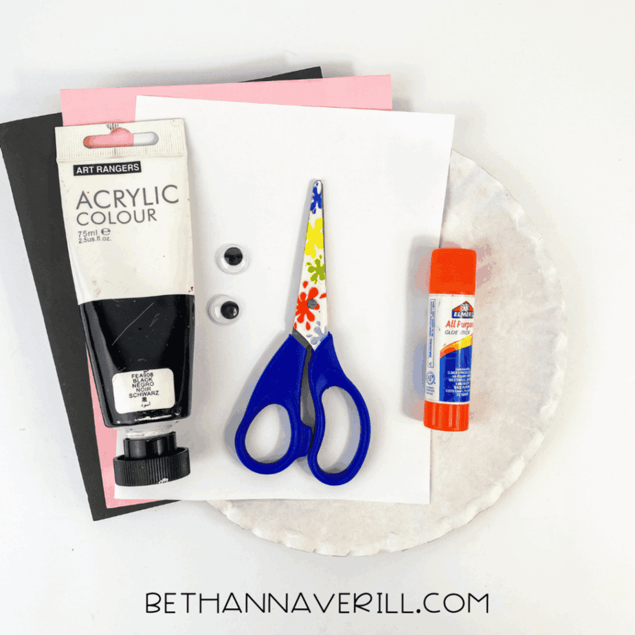 Materials laid out including paint, glue stick, scissors, googly eyes, construction paper, and a paper plate.