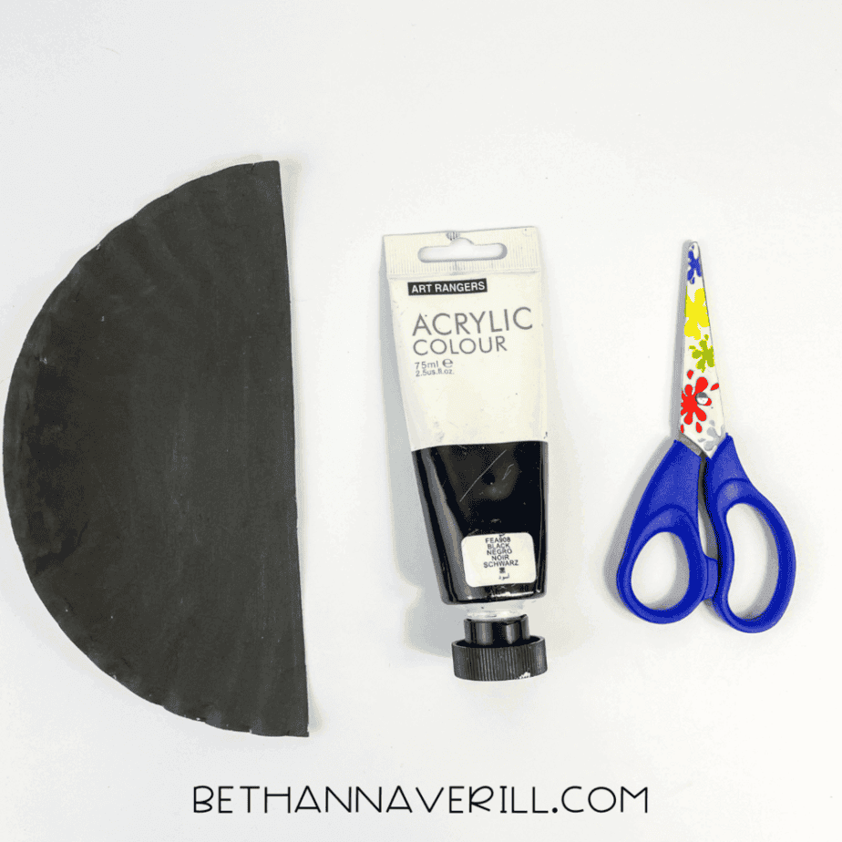 Half of a paper plate painted black next to scissors and black paint.