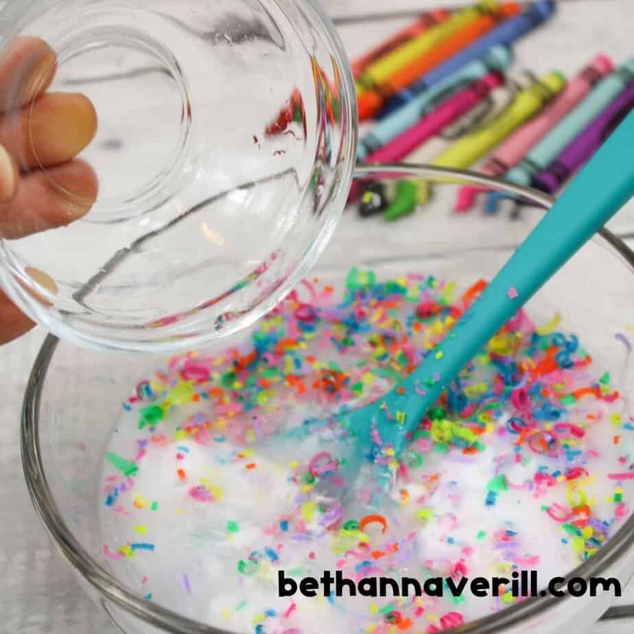Pouring clear contact solution into a bowl of glue and crayon shavings mixture to activate crayon slime.
