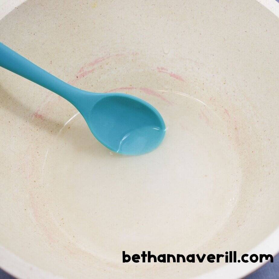 A bowl with clear liquid and a teal spoon in the center, likely water and baking soda mixed together as the base for slime-making.