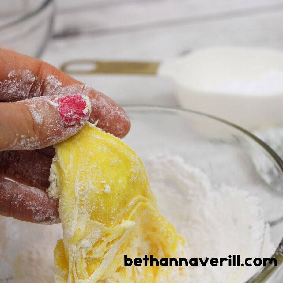Hand kneading yellow Starburst slime in a bowl of powdered sugar to achieve the perfect soft and stretchy consistency.