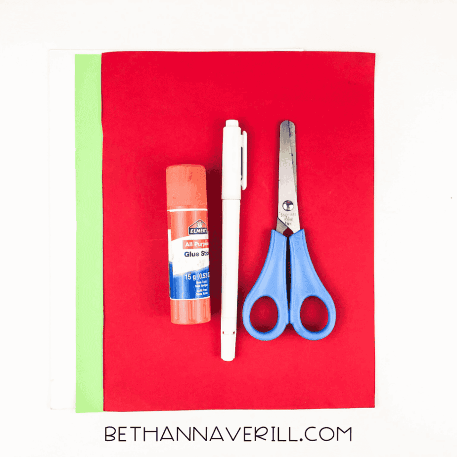 Supplies for the strawberry handprint craft including red and green paper, glue stick, scissors, and marker