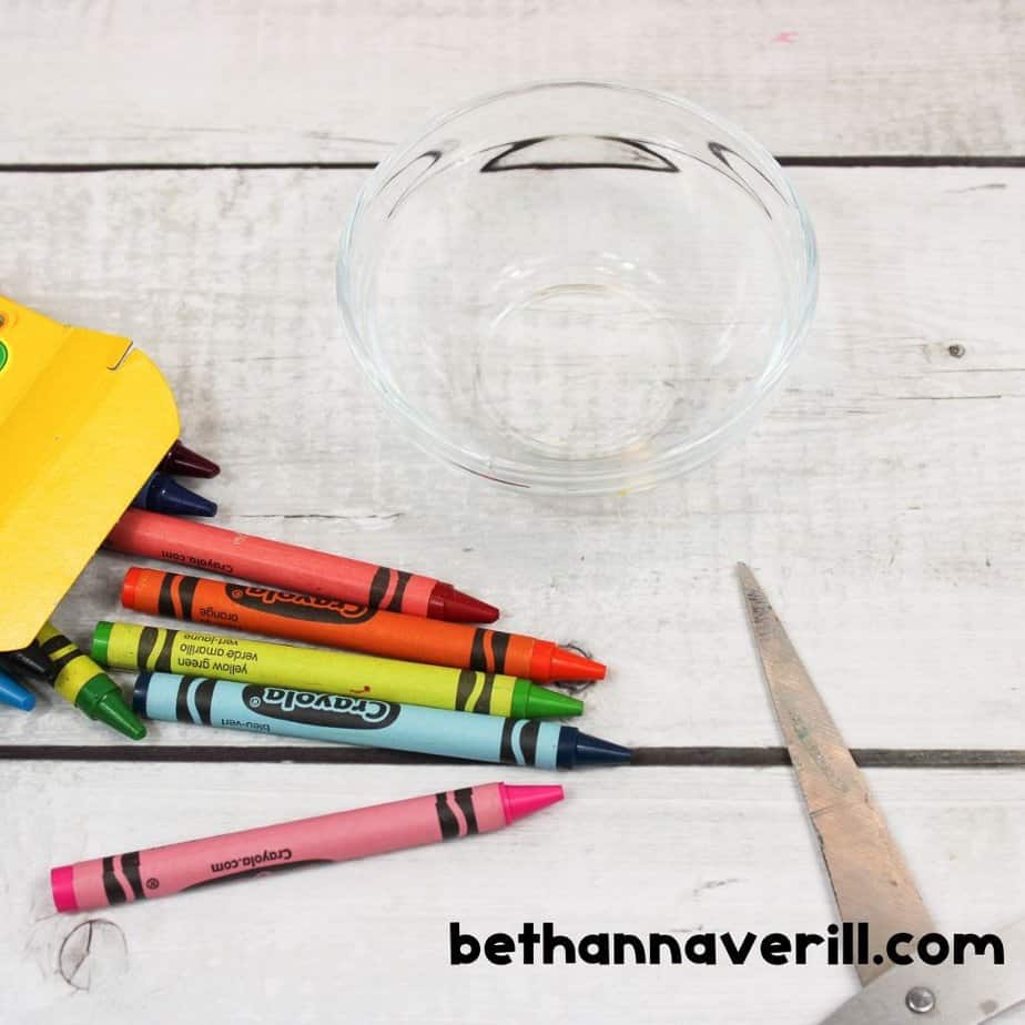 Unwrapped Crayola crayons arranged beside an empty glass bowl and a pair of scissors, ready to be shaved for making crayon slime.