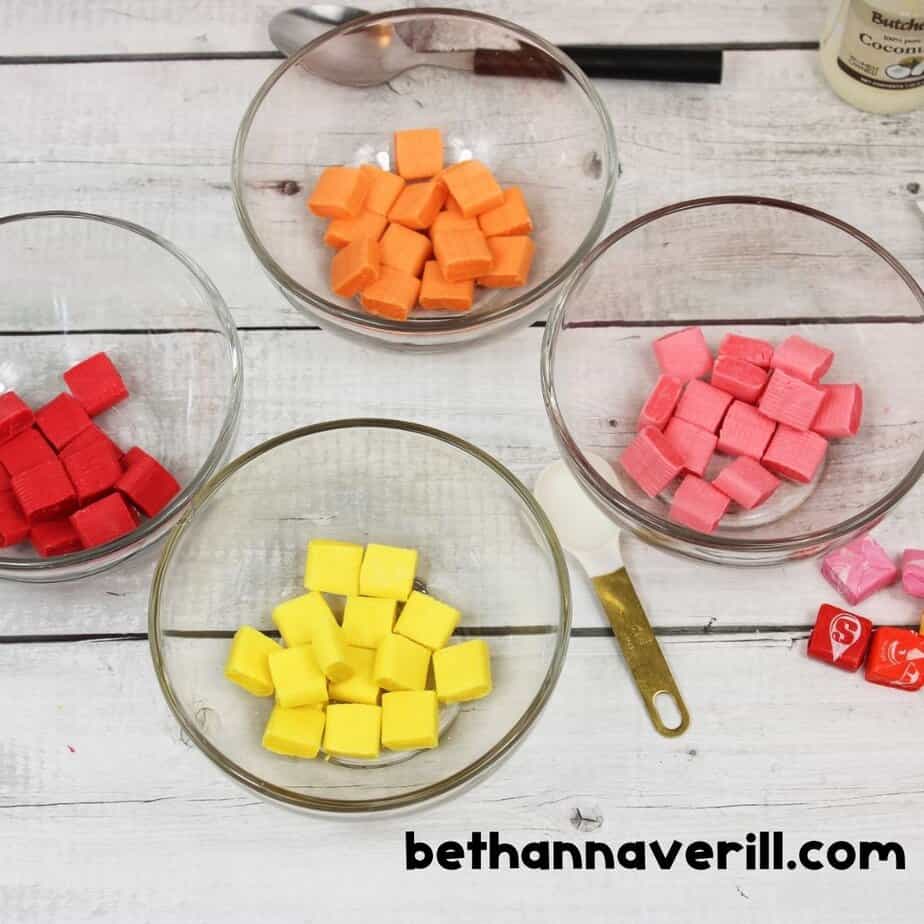 Unwrapped Starburst candies sorted by color into bowls for making vibrant edible slime, with utensils and ingredients nearby.
