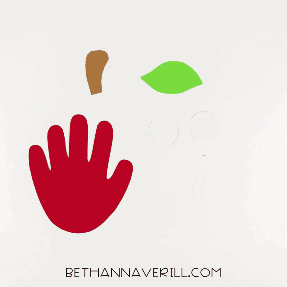 Cut pieces for the apple craft: red handprint, stem, leaf, eyes, and highlight.