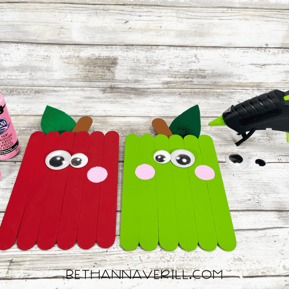 Red and green apples with googly eyes and pink cheeks being glued on.