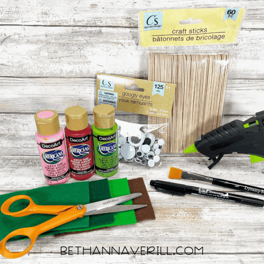 Craft supplies laid out: paint, felt sheets, googly eyes, craft sticks, scissors, glue gun, and paintbrush.