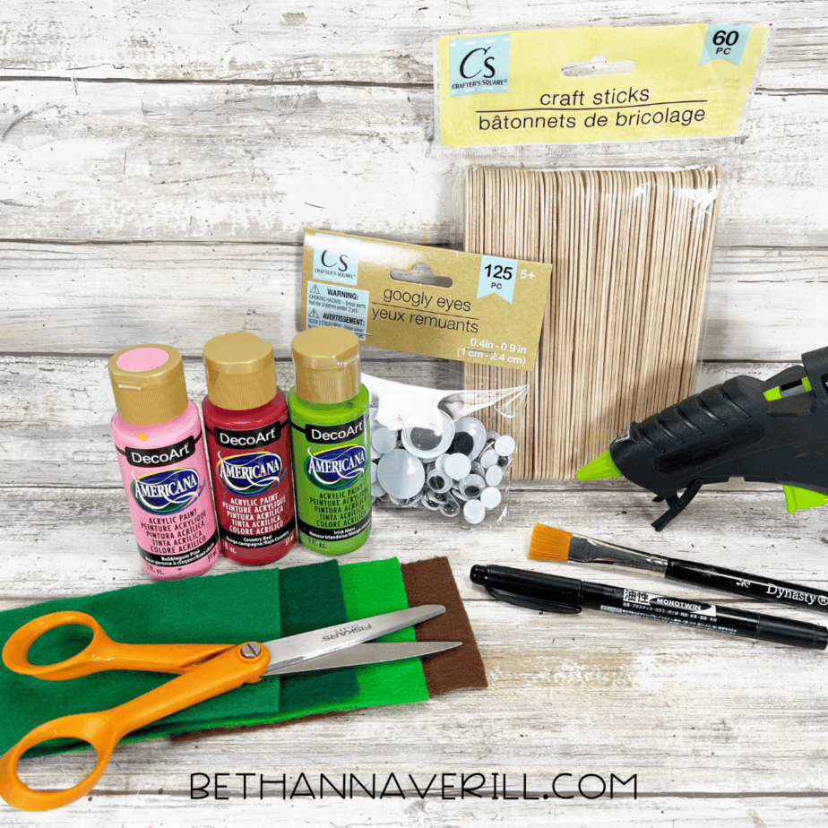 Craft supplies laid out: paint, felt sheets, googly eyes, craft sticks, scissors, glue gun, and paintbrush.