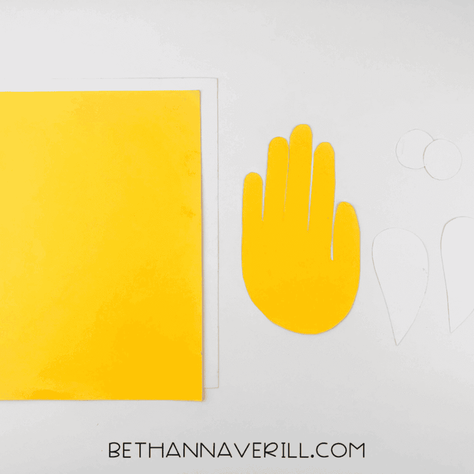 Yellow handprint cut out next to white paper pieces for eyes and wings.