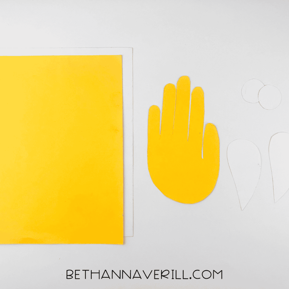 Yellow handprint cut out next to white paper pieces for eyes and wings.