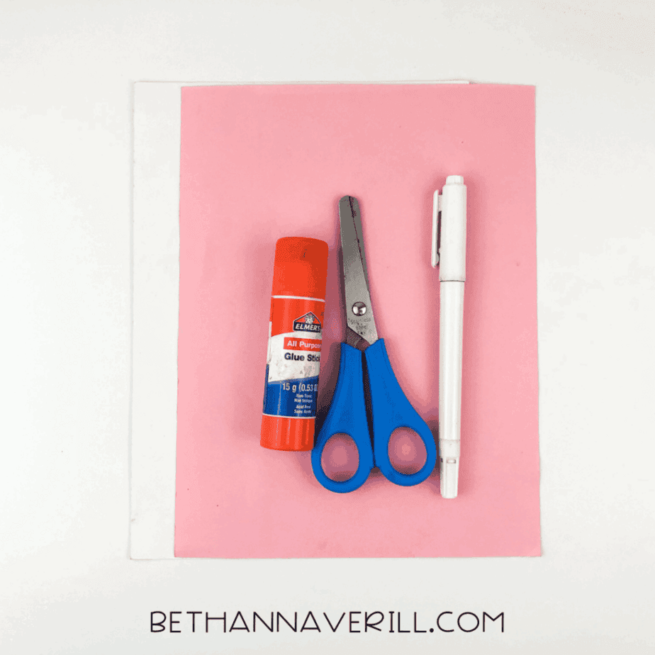 Craft supplies laid out: pink and white paper, glue stick, scissors, marker.