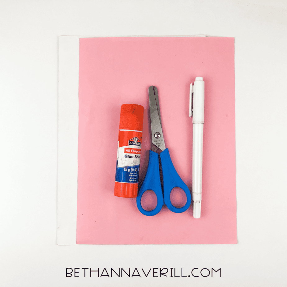 Craft supplies laid out: pink and white paper, glue stick, scissors, marker.