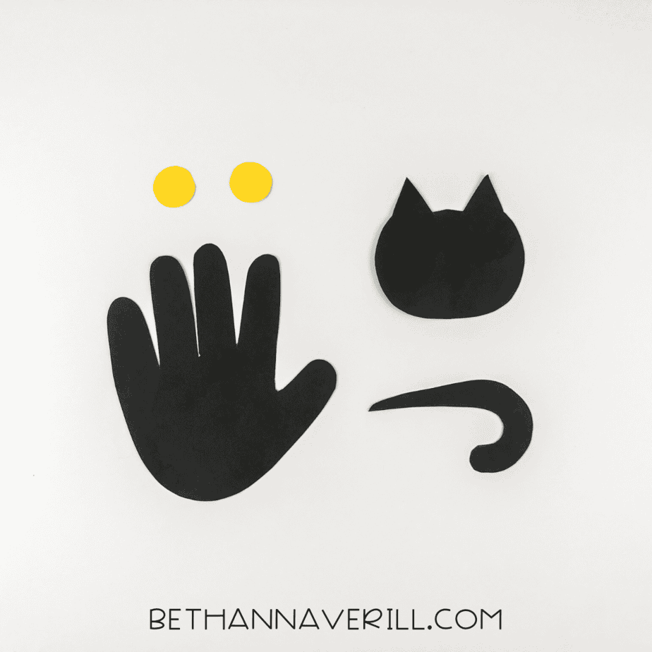 Cutout shapes: black handprint, black cat head, black tail, and yellow eyes