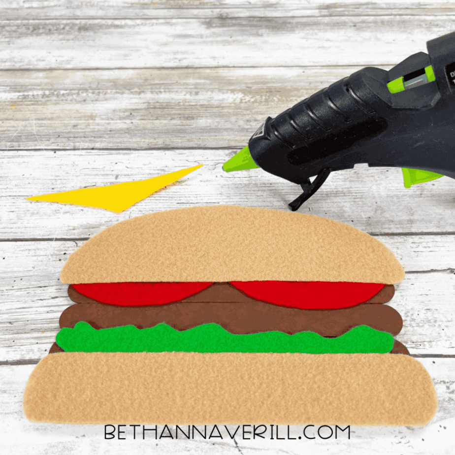 Burger layered with tomato, lettuce, and bun, glue gun nearby.