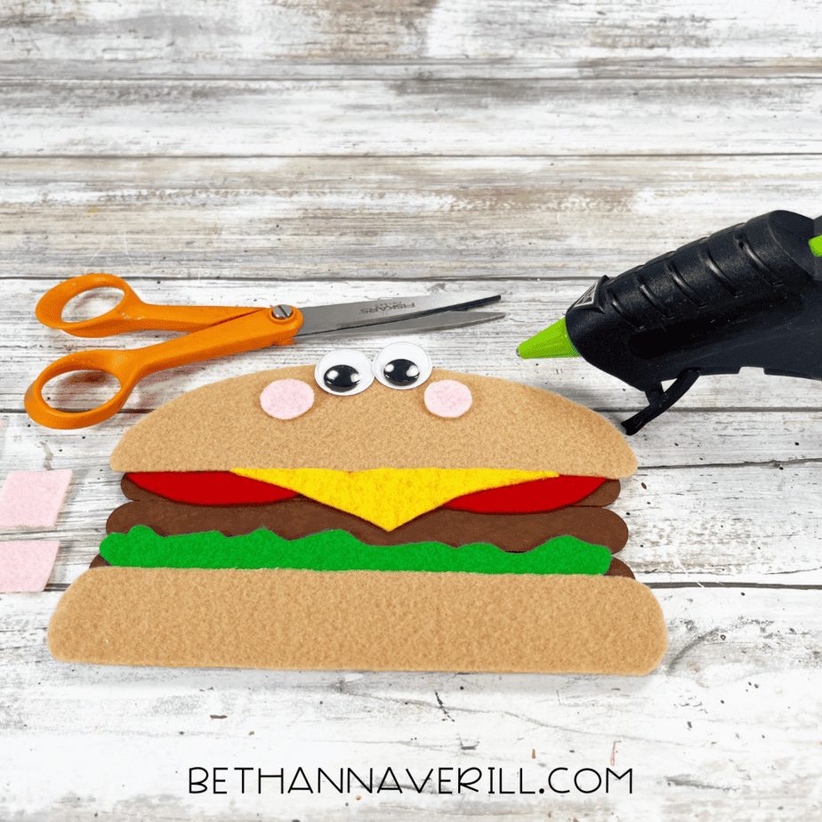 Cheeseburger with googly eyes and pink cheeks glued on top bun.