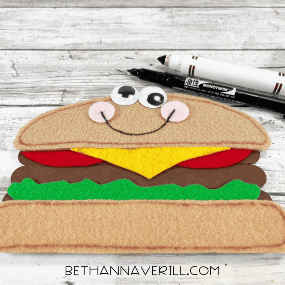 Cheeseburger with googly eyes, cheeks, and smile drawn on with marker.