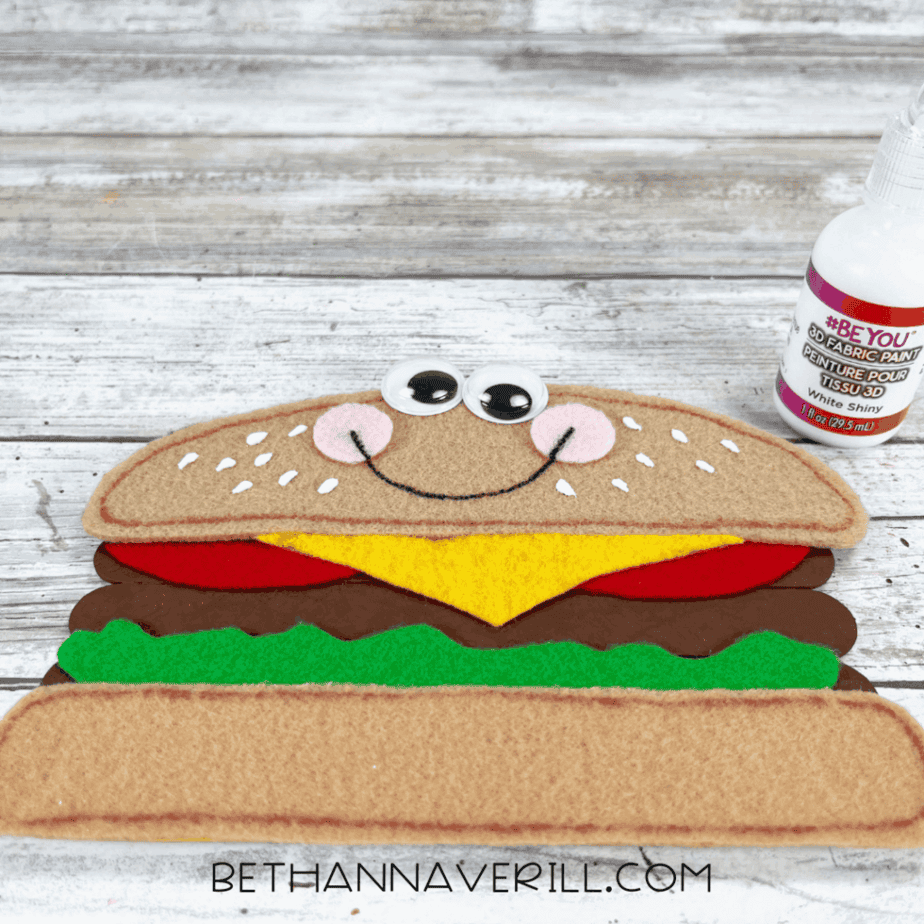Cheeseburger with googly eyes, cheeks, and smile drawn on with marker.