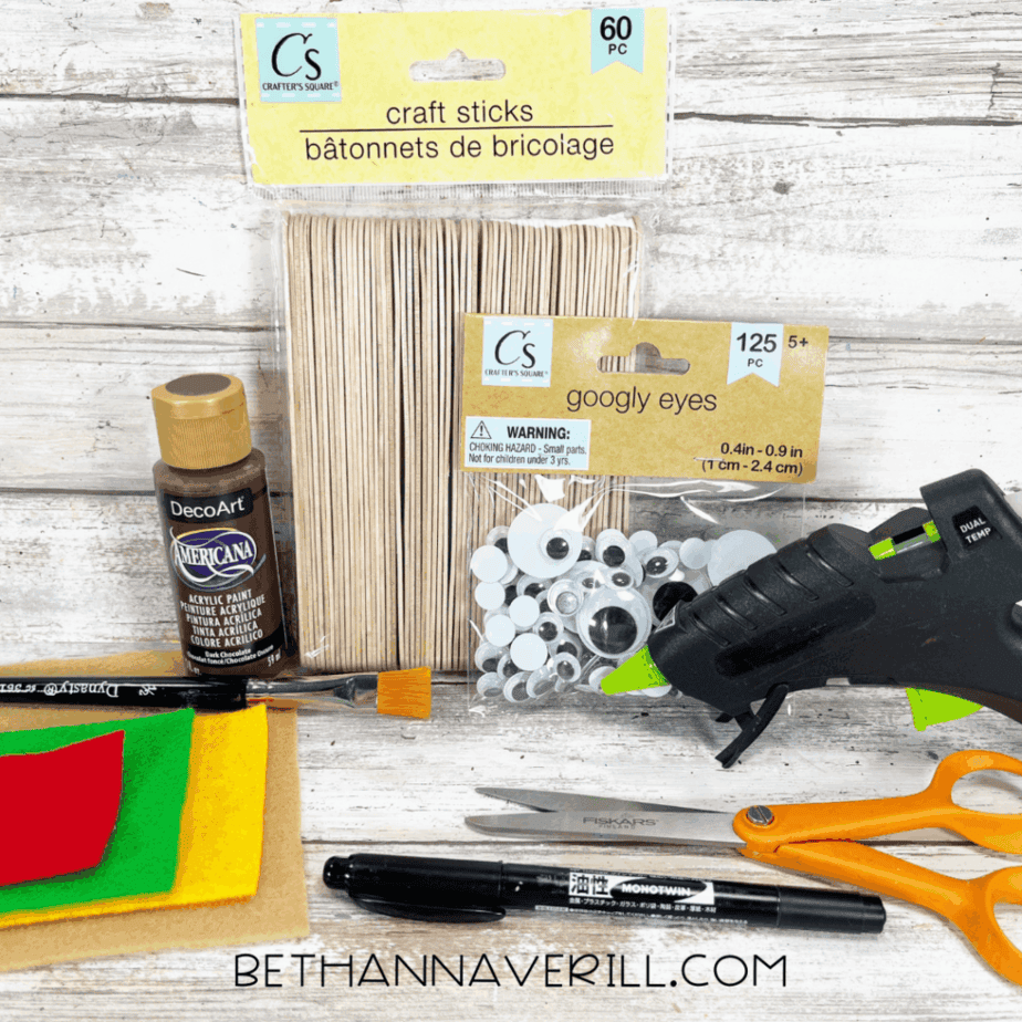 Cheeseburger popsicle stick craft supplies including paint, felt, googly eyes, glue gun, and scissors.