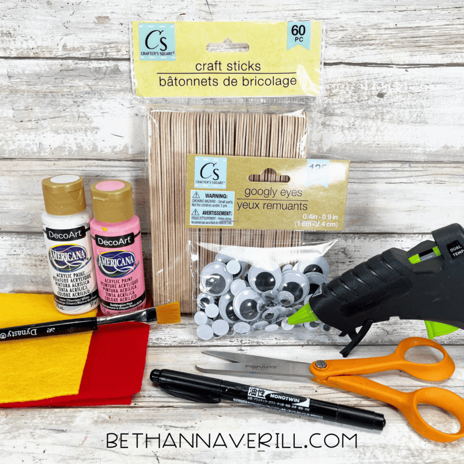 Craft supplies for popsicle stick chicken including felt, paint, googly eyes, and glue gun.