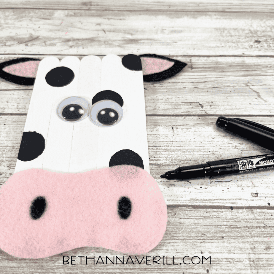 Black marker adding nostrils to pink felt snout on cow craft.